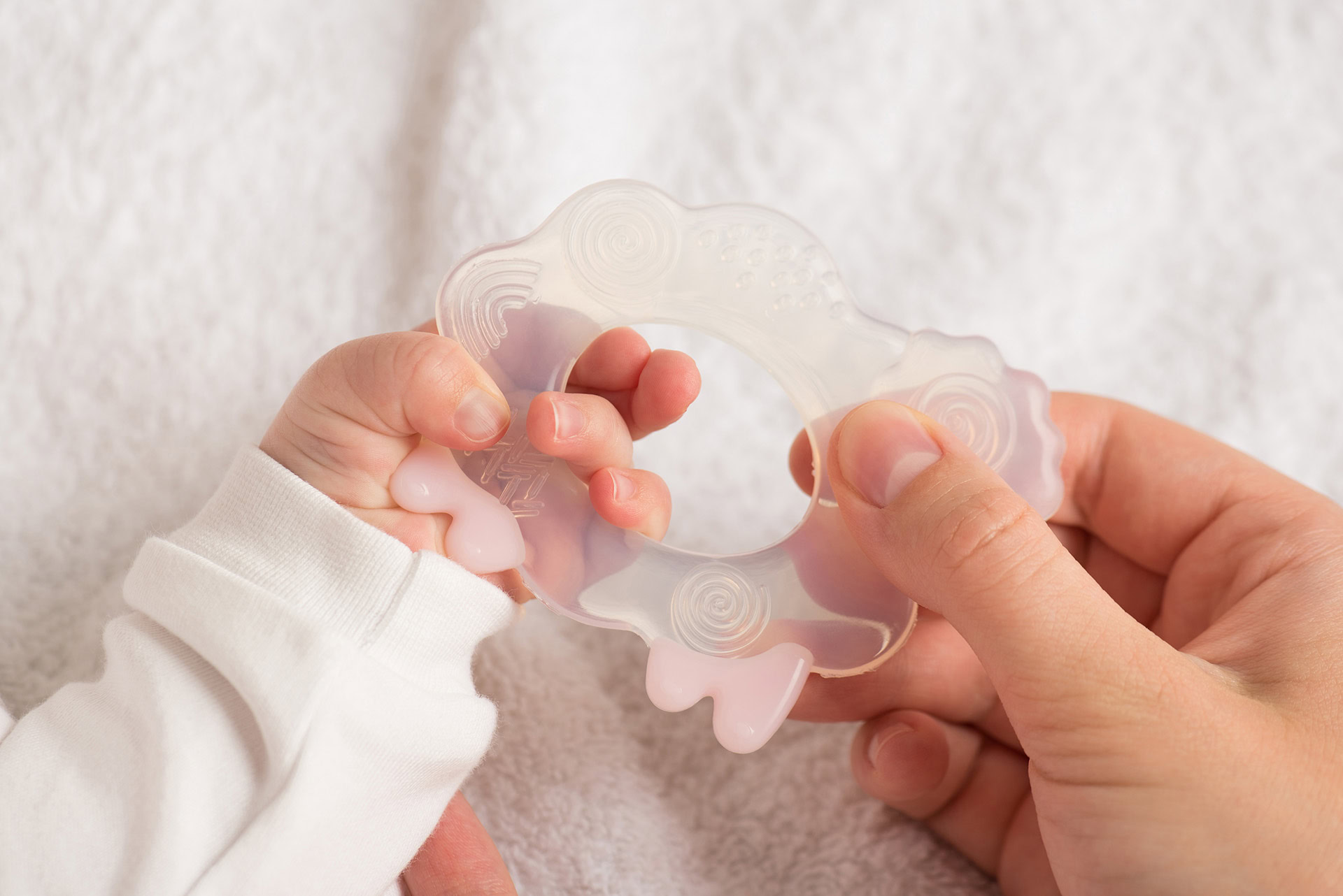 closeup photo baby s mother s hands holding transparent teether toy lamb isolated white textile background